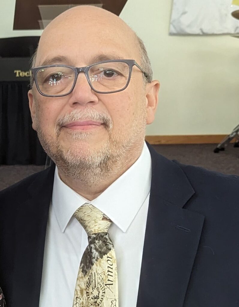 A man in glasses and a suit standing next to drums.